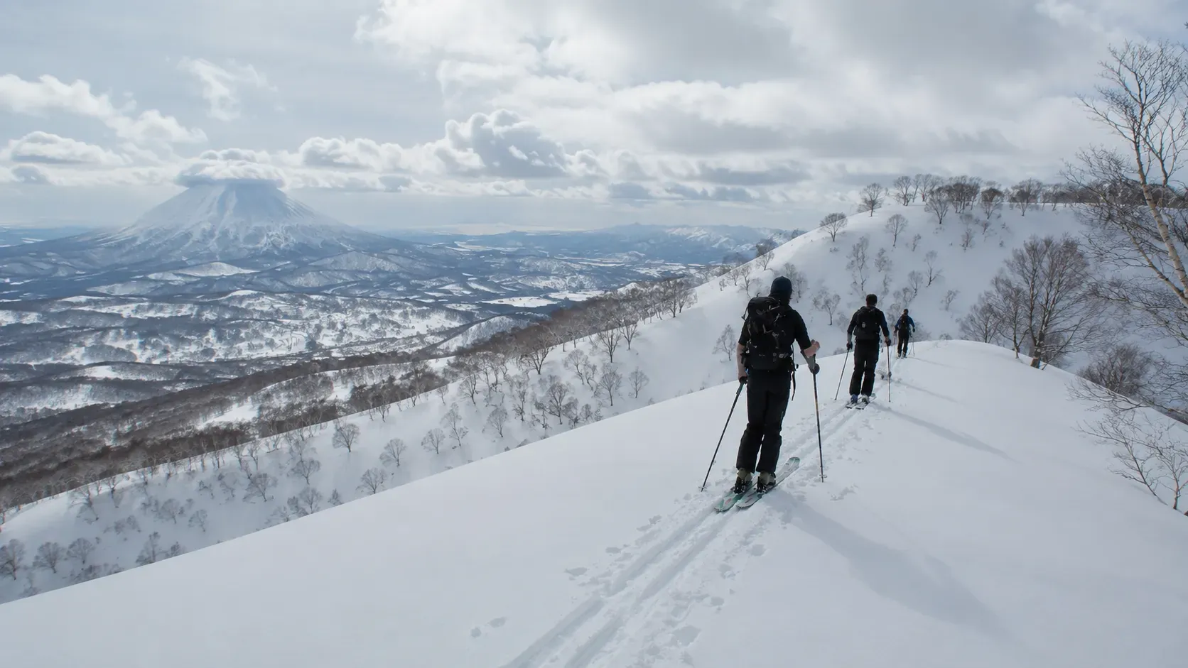Group skinning up a snowy ridge with Mount Yotei behind them