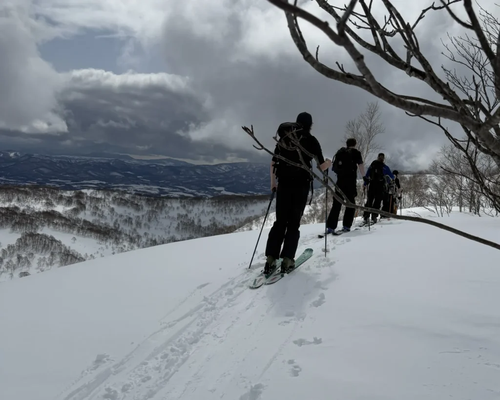 Group touring in single file along a ridge in the Niseko backcountry under storm clouds