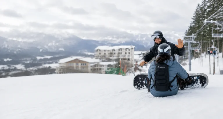 Snowboard instructor giving a high five to a beginner student sitting on a groomed slope