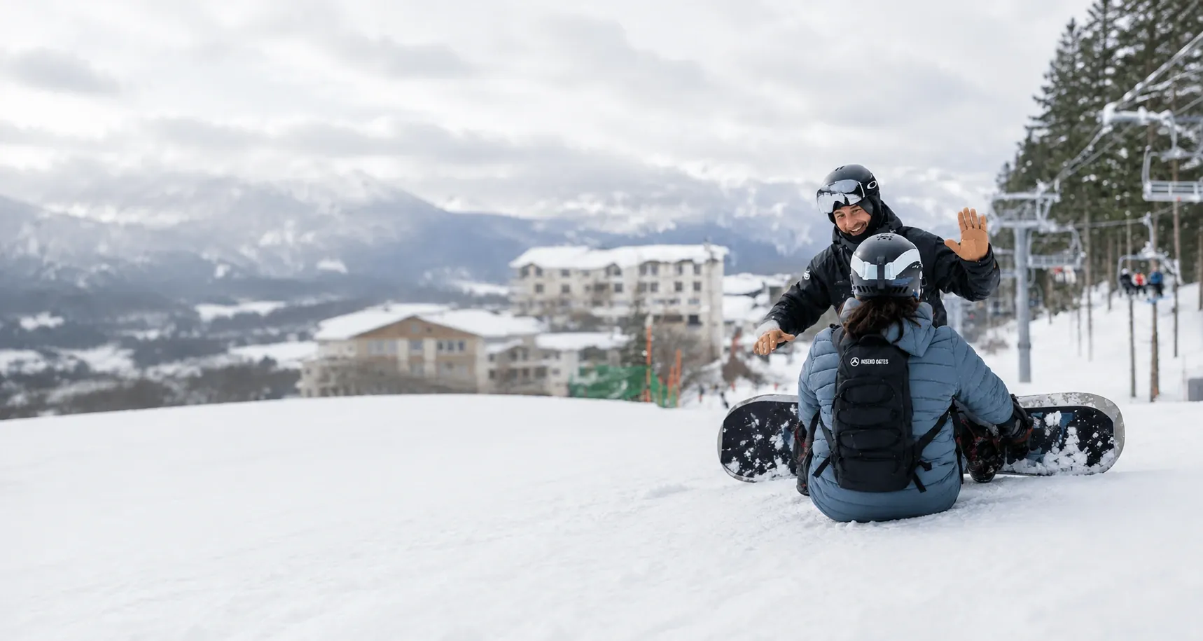 Snowboard instructor giving a high five to a beginner student sitting on a groomed slope