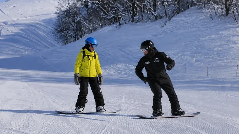 Snowboard instructor coaching a student on a groomed run in Niseko