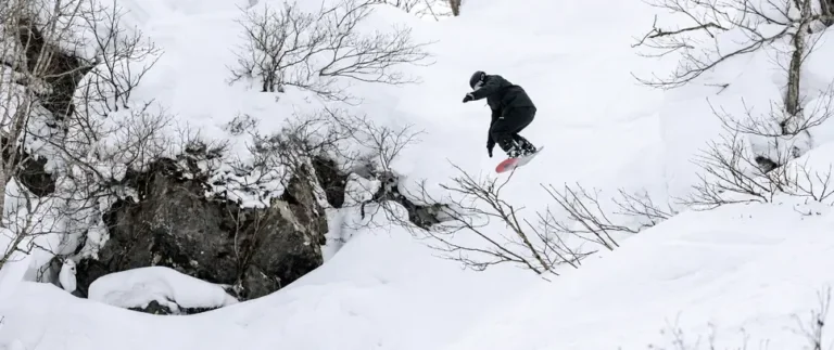 Snowboarder dropping off a snowy rock into powder between trees