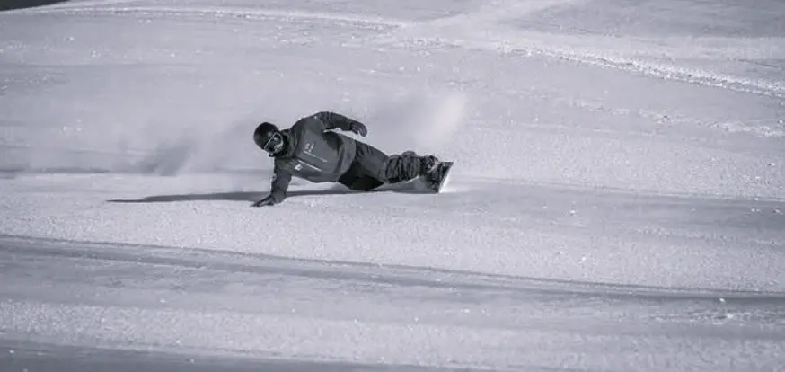 Snowboarder laying down a low heelside euro carve with a hand on the snow