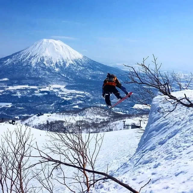 Snowboarder jumping off a snow bank with Mount Yotei in the background at Grand Hirafu
