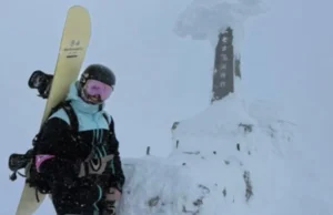 Snowboarder in pink low-light goggles carrying a powder board at the snowy summit of Mount Niseko Annupuri