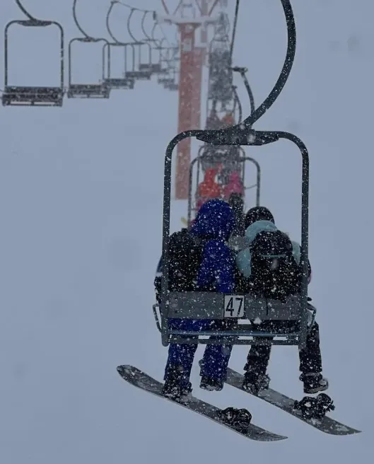 Two snowboarders riding a chairlift during heavy snowfall in Niseko