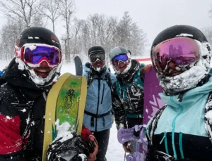 Group of snow-covered snowboarders holding their powder boards on a storm day in Japan