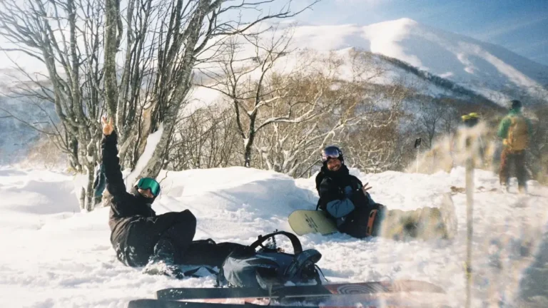 Two snowboarders relaxing in the snow on a sunny day in Niseko, shot on film