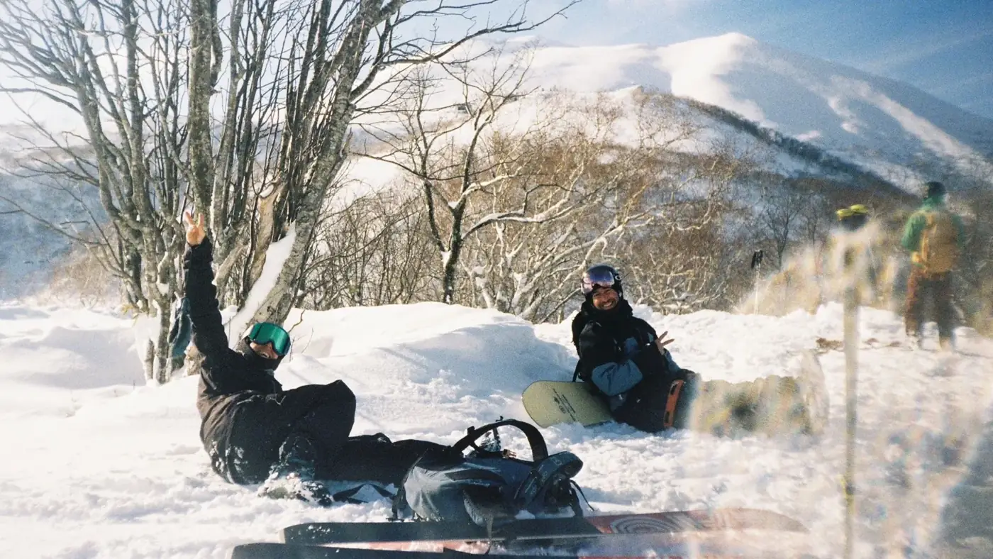 Two snowboarders relaxing in the snow on a sunny day in Niseko, shot on film
